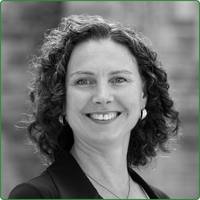 A black and white head shot of Catherine Steeves. standing outside and smiling at the camera