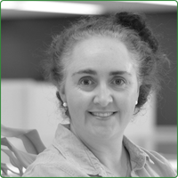 A black and white photo of Jacqueline Whyte Appleby, standing in an office space and smiling at the camera